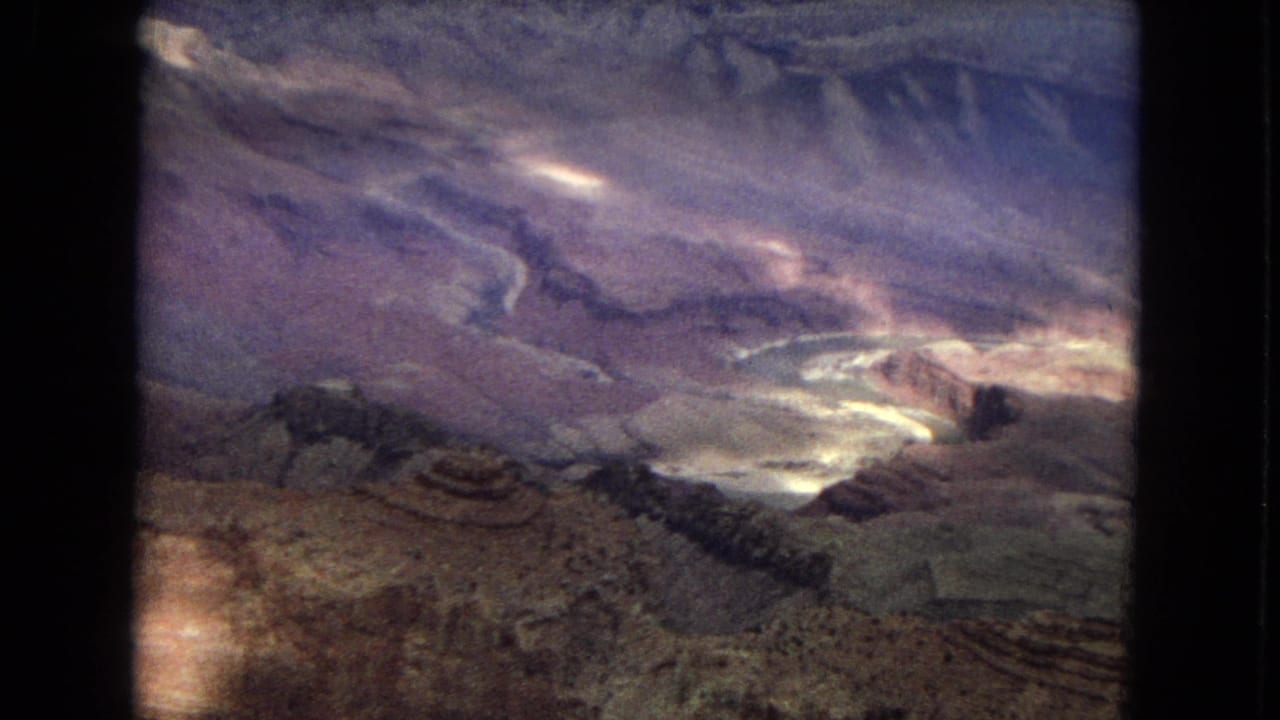 1967 8mm home-movie view across an Arizona canyon, showing broad cliffs, a winding river channel below, muted desert colors, and visible film-gate edges.