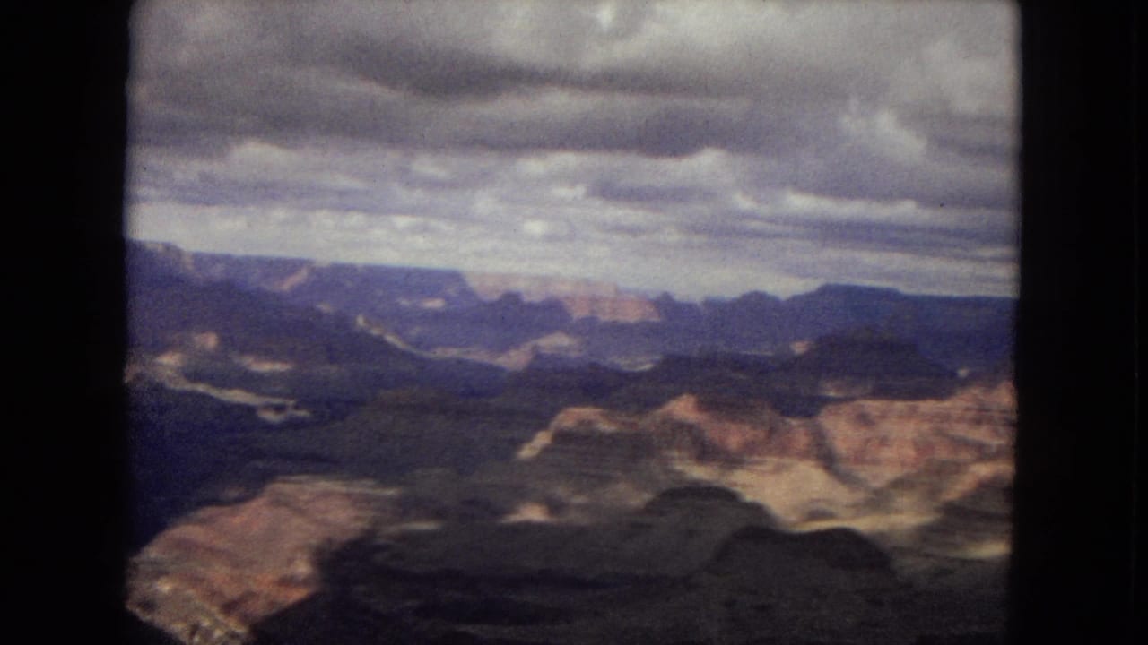 Wide canyon panorama with distant cliffs and cloud shadows.