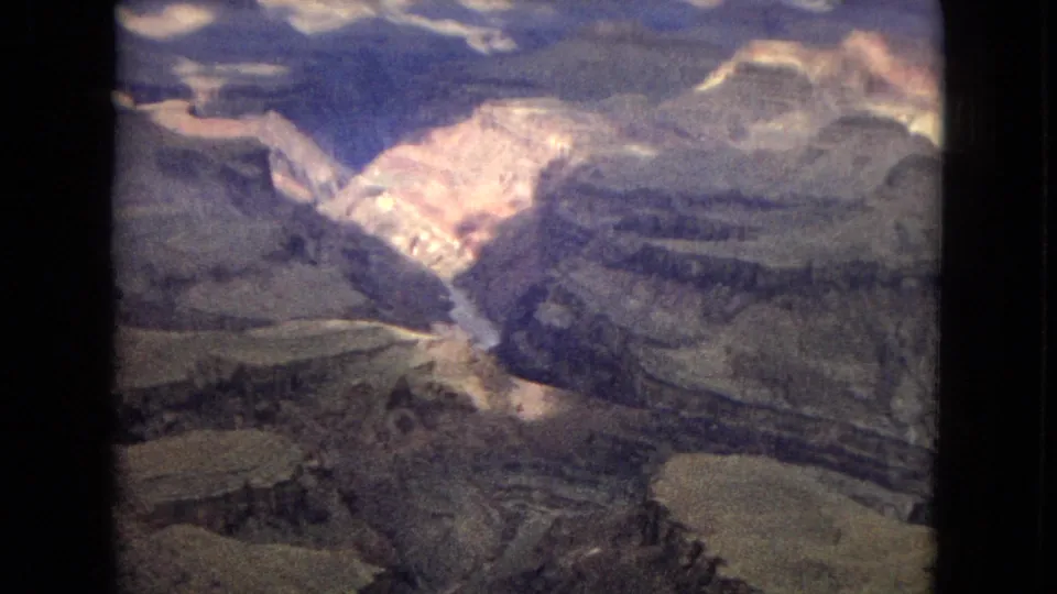 1967 Grand Canyon home-movie frame with sunlit rock formations, deep ravines, layered plateaus, and a river channel far below.