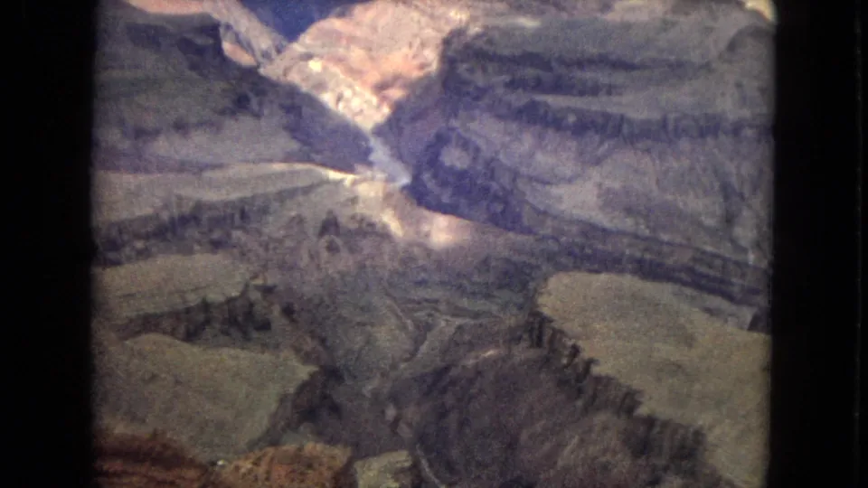1967 Arizona home-movie frame showing a broad Grand Canyon view with layered rock walls, a deep central chasm, and soft 8mm color rendering.