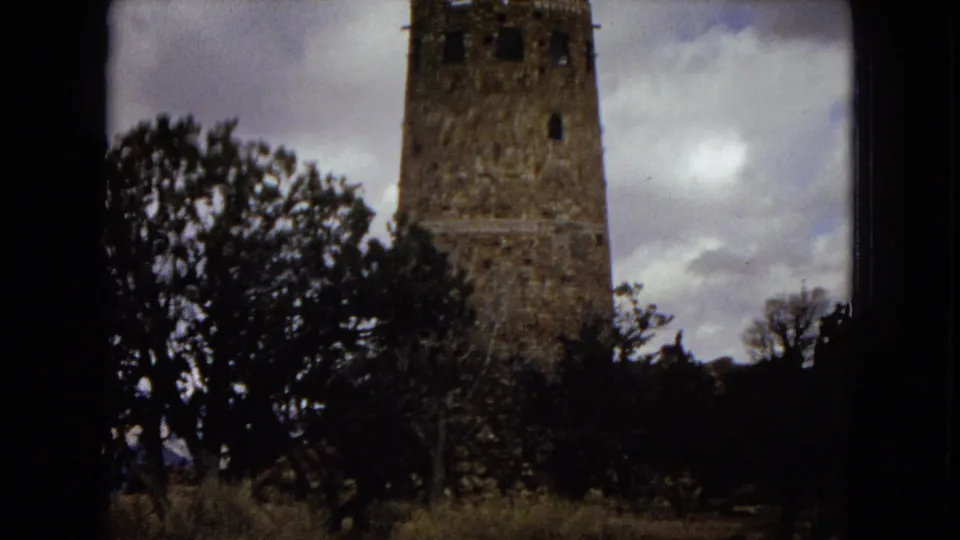 1967 Arizona travel frame showing a closer view of a tall historic stone tower, with trees and brush partially obscuring the lower structure.