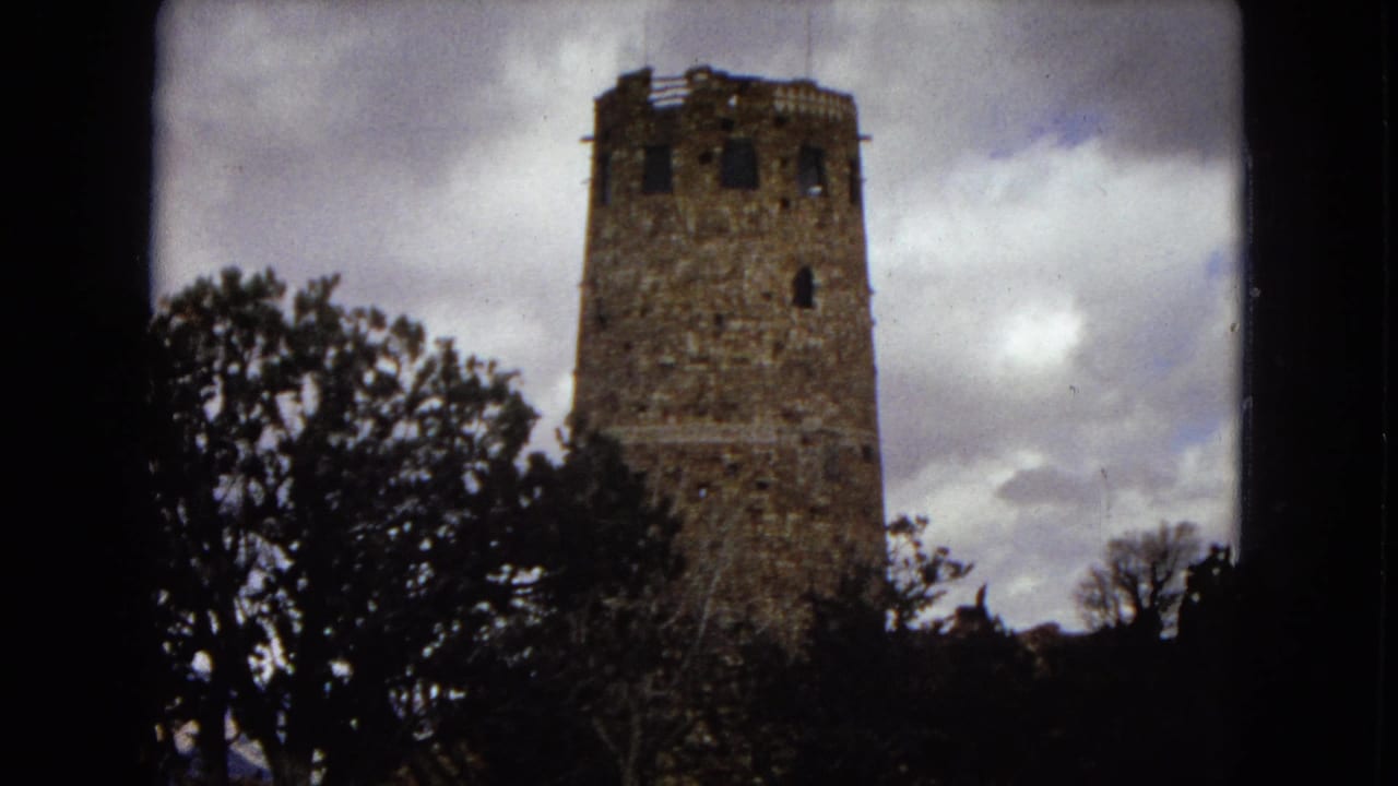1967 Arizona 8mm home-movie frame showing a rough stone tower among silhouetted trees beneath a cloudy sky.