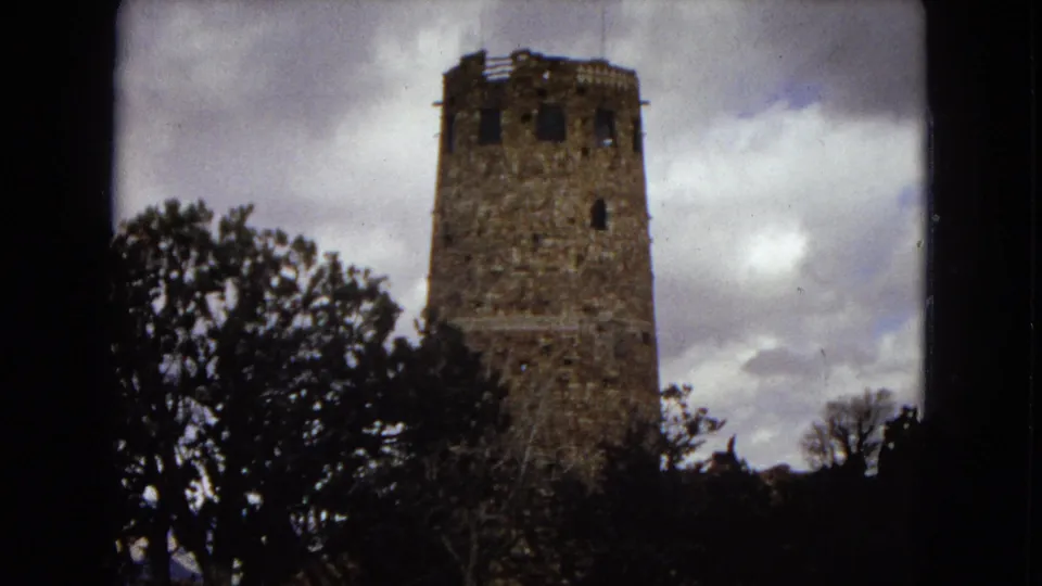 1967 Arizona 8mm home-movie frame showing a rough stone tower among silhouetted trees beneath a cloudy sky.