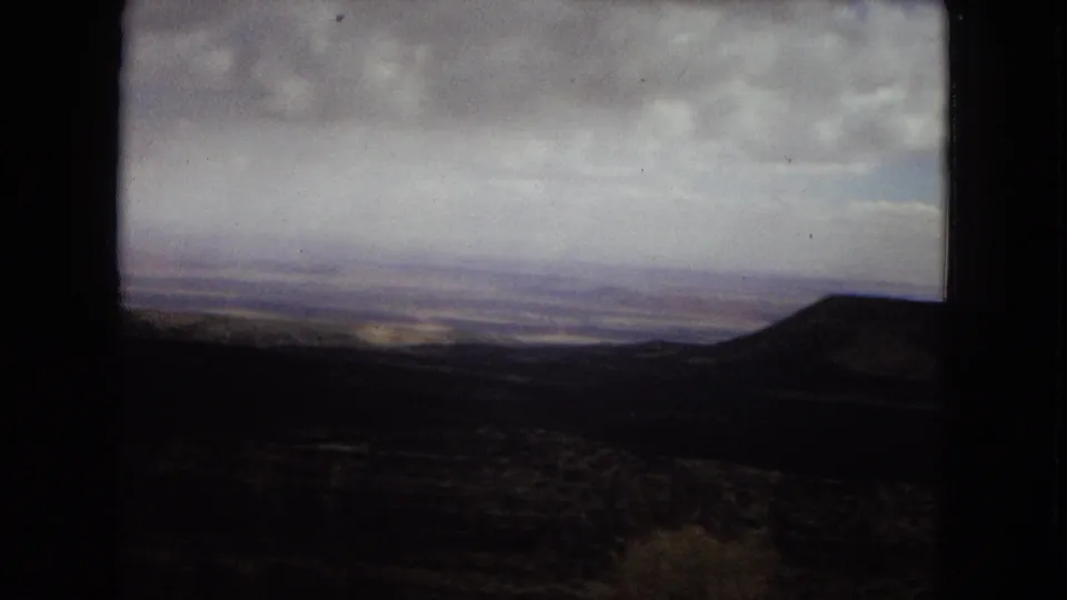 1967 Arizona 8mm frame showing a broad distant vista with a rounded hill on the right, muted desert tones, and a cloudy sky.