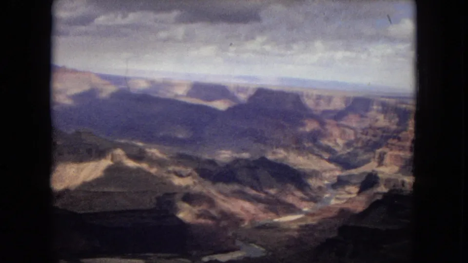 1967 8mm Arizona canyon panorama with broad rock shelves, deep shadowed valleys, and soft focus across the distant rim.