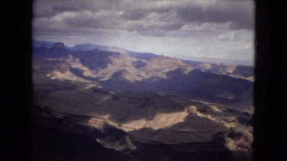 1967 8mm Arizona footage showing layered Grand Canyon formations, dark foreground ridges, and a broad cloudy sky.
