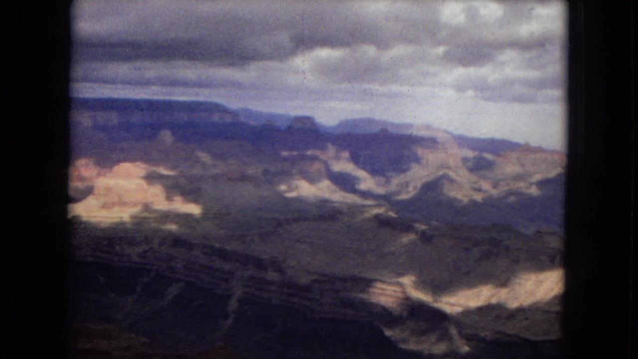 1967 8mm Arizona view across the Grand Canyon, with distant plateau edges, shadowed rock layers, and patches of pale sunlight.