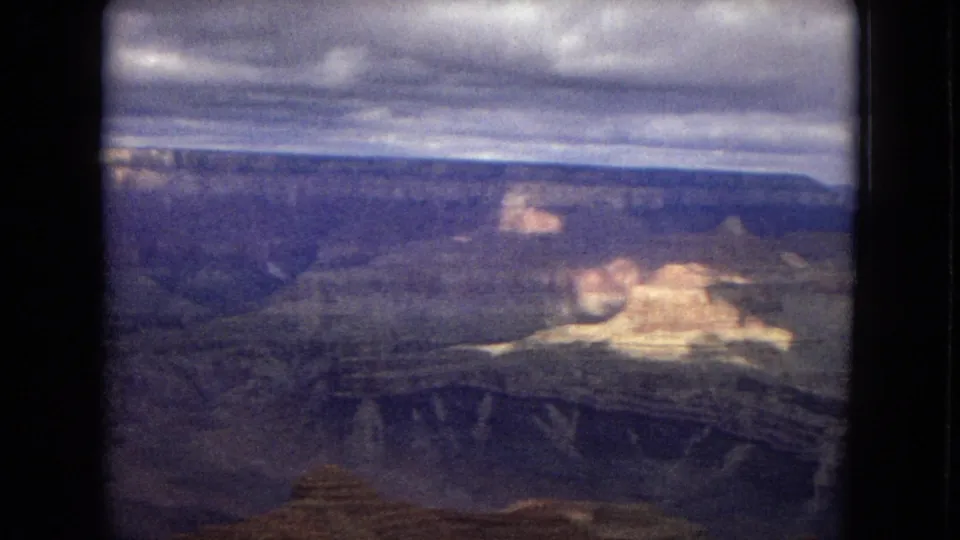 1967 8mm Arizona footage showing sunlit Grand Canyon rock forms against darker canyon walls and a heavy cloud bank above.