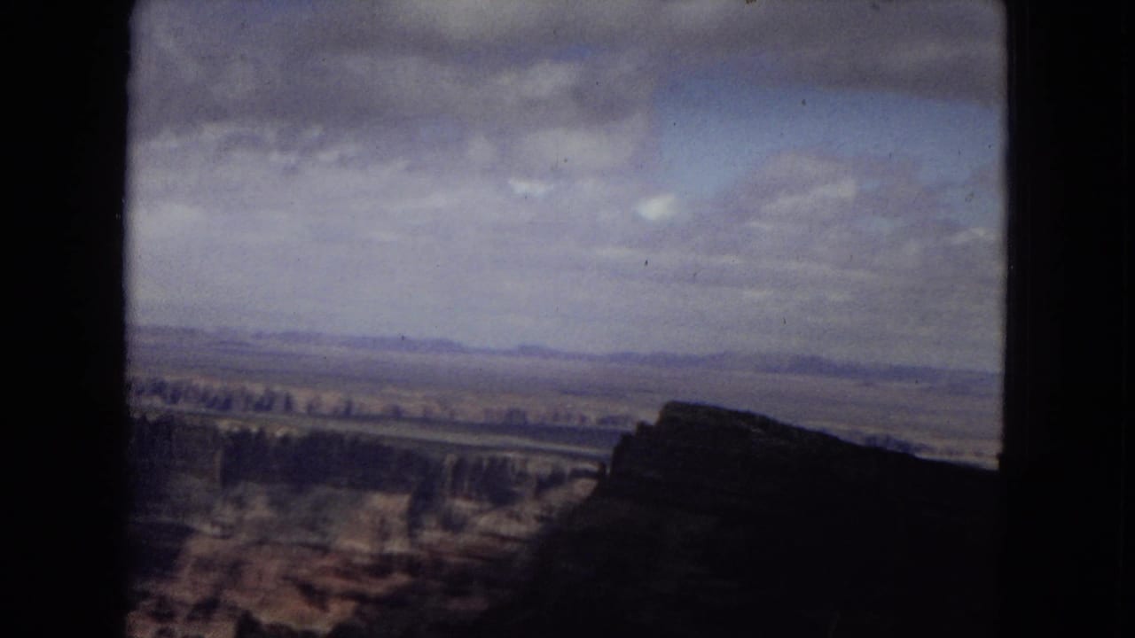 1967 Arizona 8mm view across the Grand Canyon, with a shadowed canyon edge in front and pale clouds over distant layered terrain.