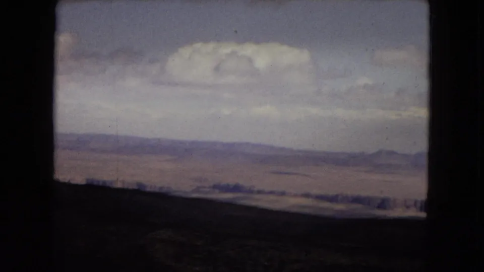 1967 Arizona home-movie view across the Grand Canyon, with a dark overlook edge, layered distance, and a bright cloud suspended over the horizon.