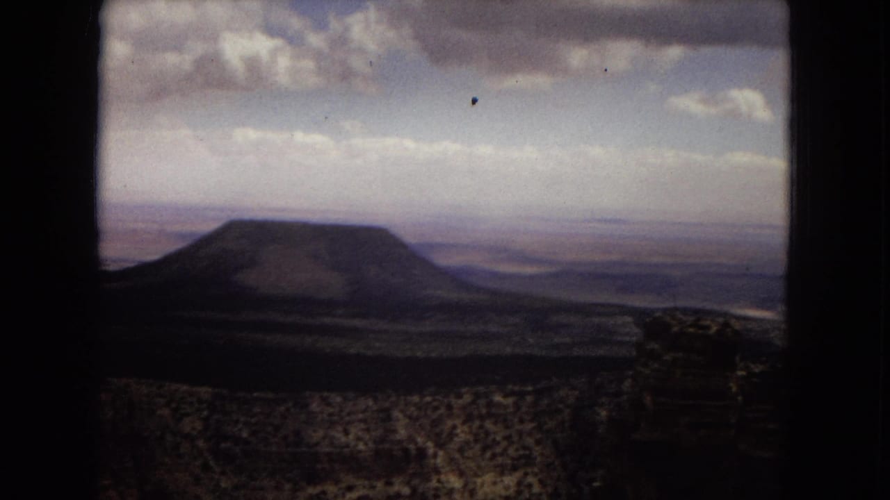 1967 home-movie view in the United States showing a flat-topped butte or mesa across open desert terrain beneath layered clouds.