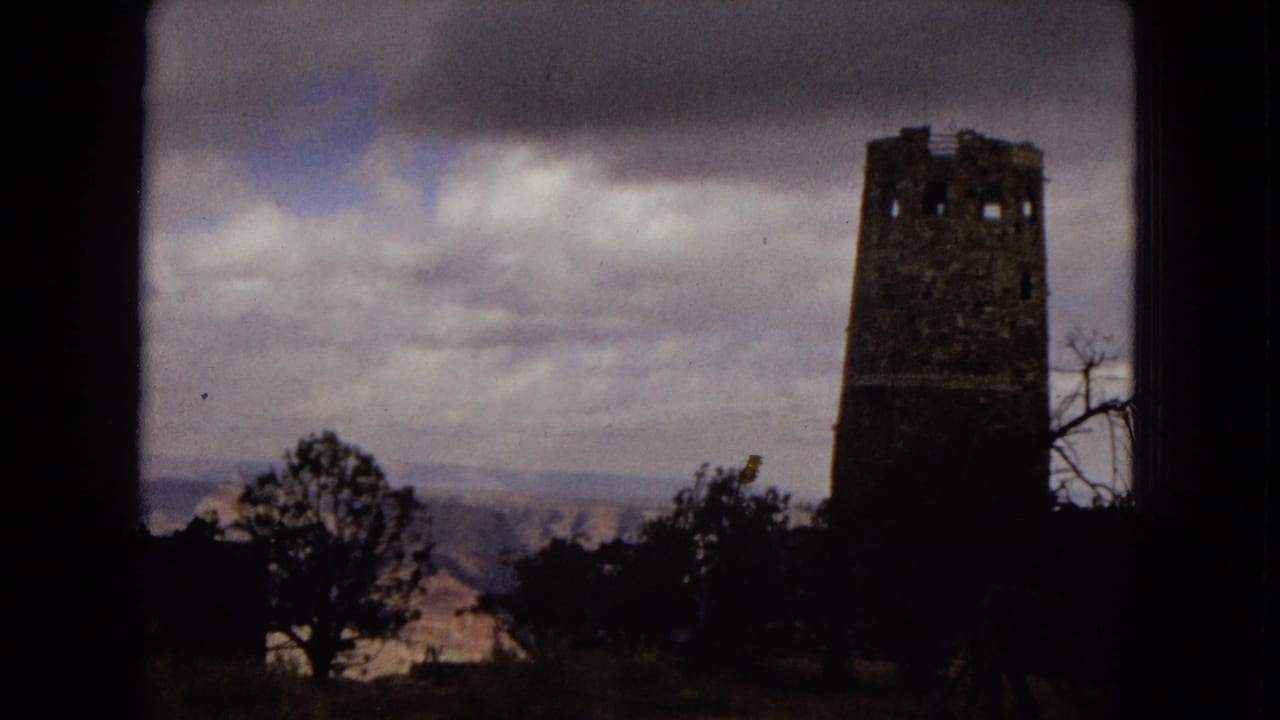 1967 Arizona 8mm travel frame showing the Desert View Watchtower at Grand Canyon National Park beyond silhouetted trees and a cloudy sky.