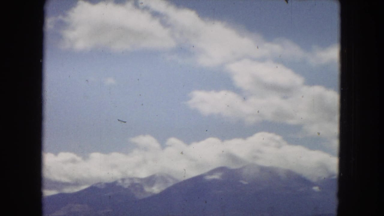 1967 Arizona 8mm travel footage showing a distant mountain ridge under a blue, cloud-filled sky, with dark window or film-gate edges at the sides.