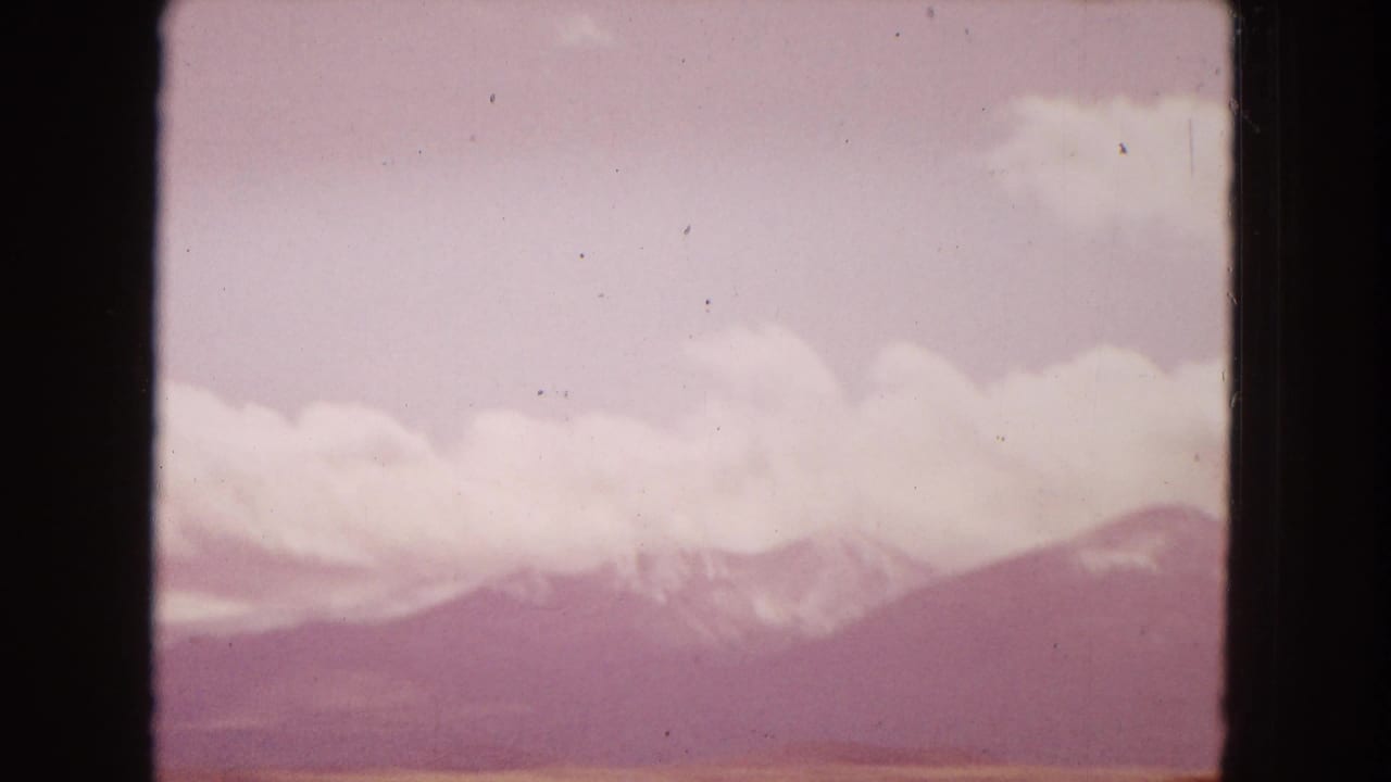 Magenta-tinted view of clouds over a distant mountain range.