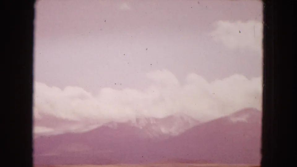 Color-shifted 8mm frame from the Arizona travel clip, showing a pale cloud bank over distant mountains with visible film dust and gate edges.