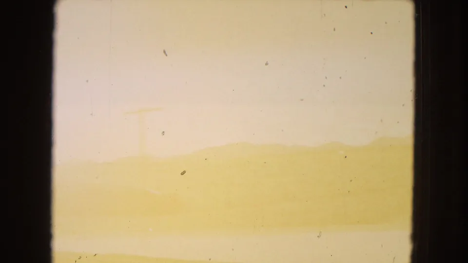 Faded 8mm frame from the Arizona landscape clip showing a low desert horizon beneath a pale sky, with subdued detail and visible film specks.