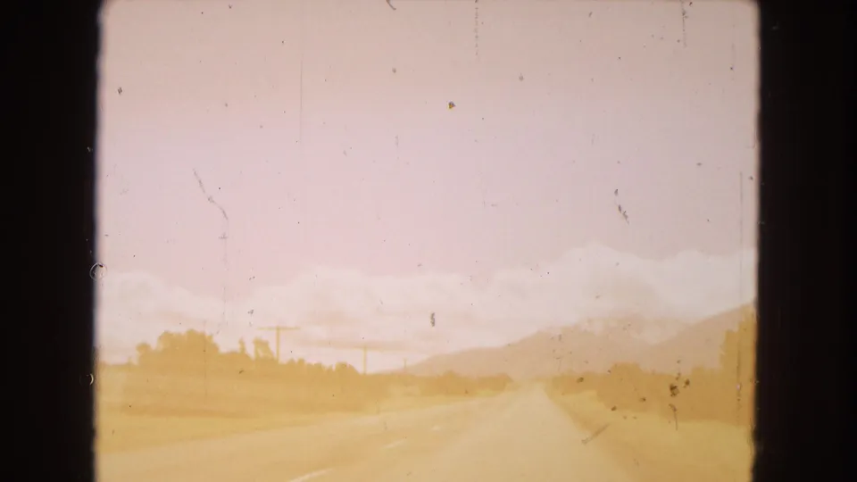 Forward-facing 8mm road view in Arizona, with the highway stretching into a sunlit desert landscape, low vegetation, utility poles, and hazy mountains beyond.