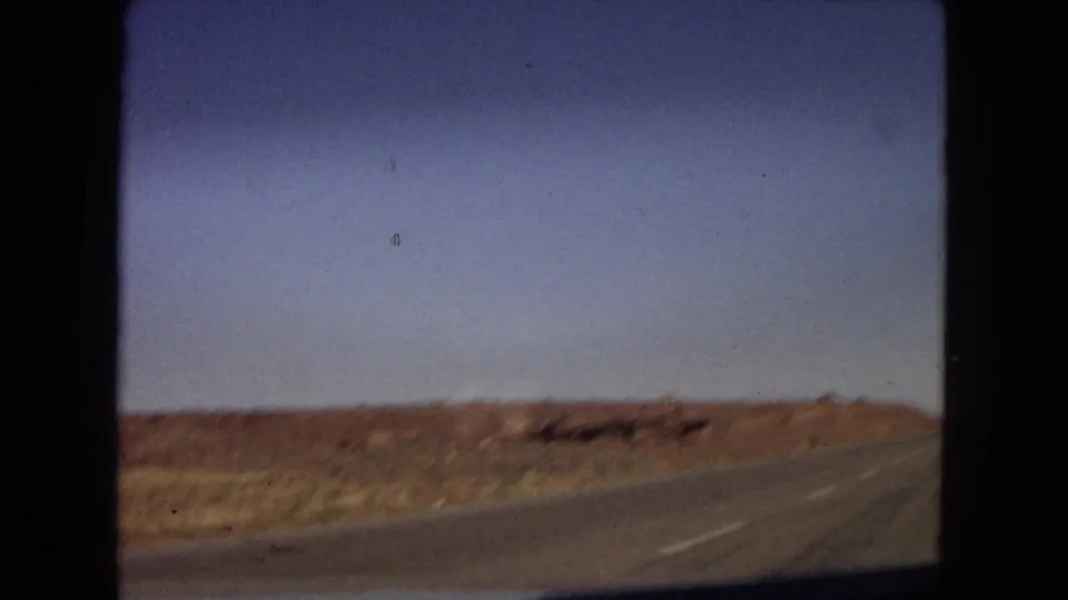 The final frame shows a paved highway curving through open arid terrain, with low reddish hills, sparse scrub, and a clear blue sky in metadata-supported Arizona footage.
