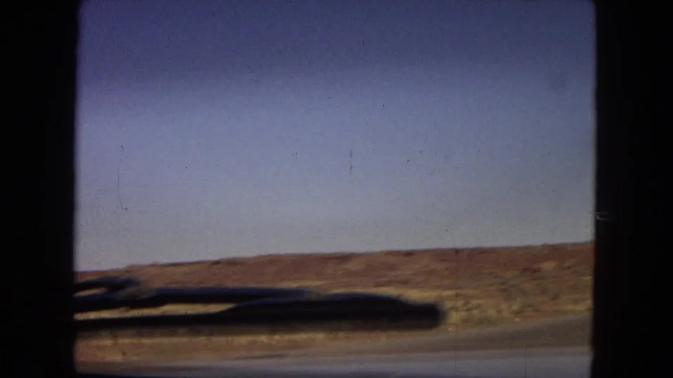 1967 Arizona 8mm frame showing a moving-car view across dry desert terrain beside an open highway under a clear blue sky.