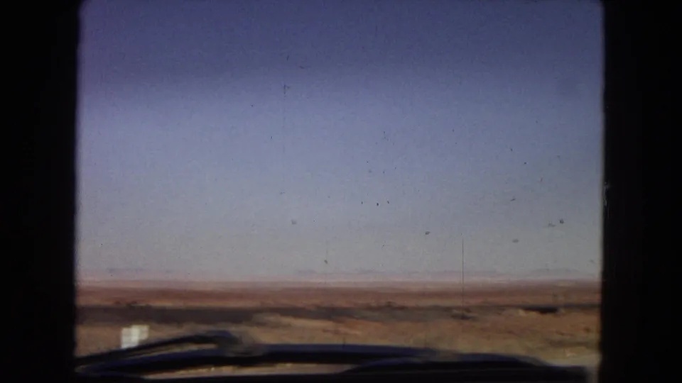1967 Arizona desert horizon viewed from a moving vehicle, with windshield wipers and dark window framing visible in the foreground.