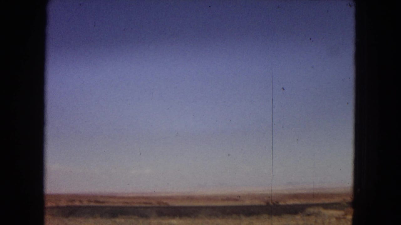 Sparse Arizona desert landscape under a clear sky, framed by dark vertical edges from the vehicle or film scan.