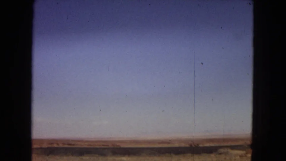 Sparse Arizona desert landscape under a clear sky, framed by dark vertical edges from the vehicle or film scan.
