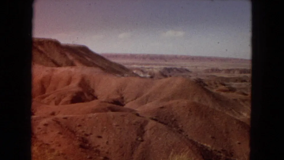 The final 1967 Arizona travel frame shows reddish eroded hills, a sloping mesa edge, dry grasses, and a broad desert valley in warm 8mm color.