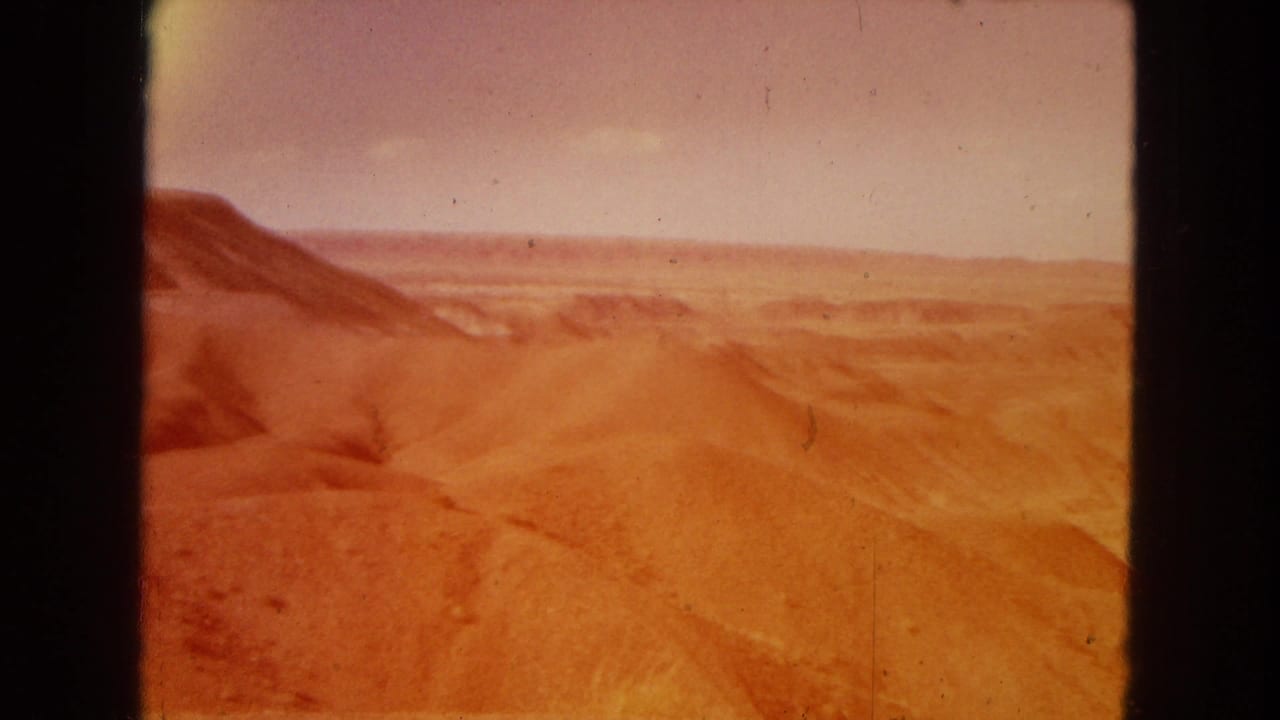 1967 8mm home-movie frame of the Painted Desert area showing reddish eroded hills and a distant horizon under daylight.
