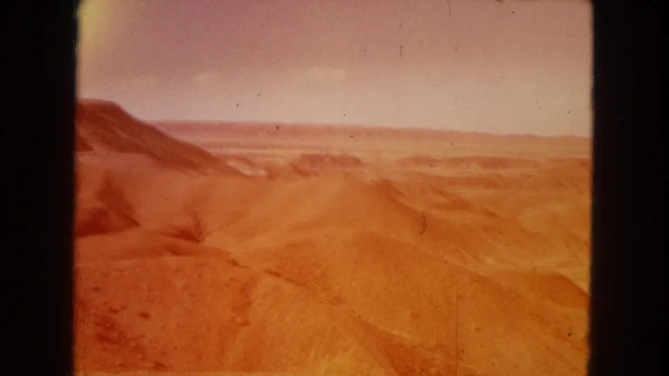 1967 8mm home-movie frame of the Painted Desert area showing reddish eroded hills and a distant horizon under daylight.