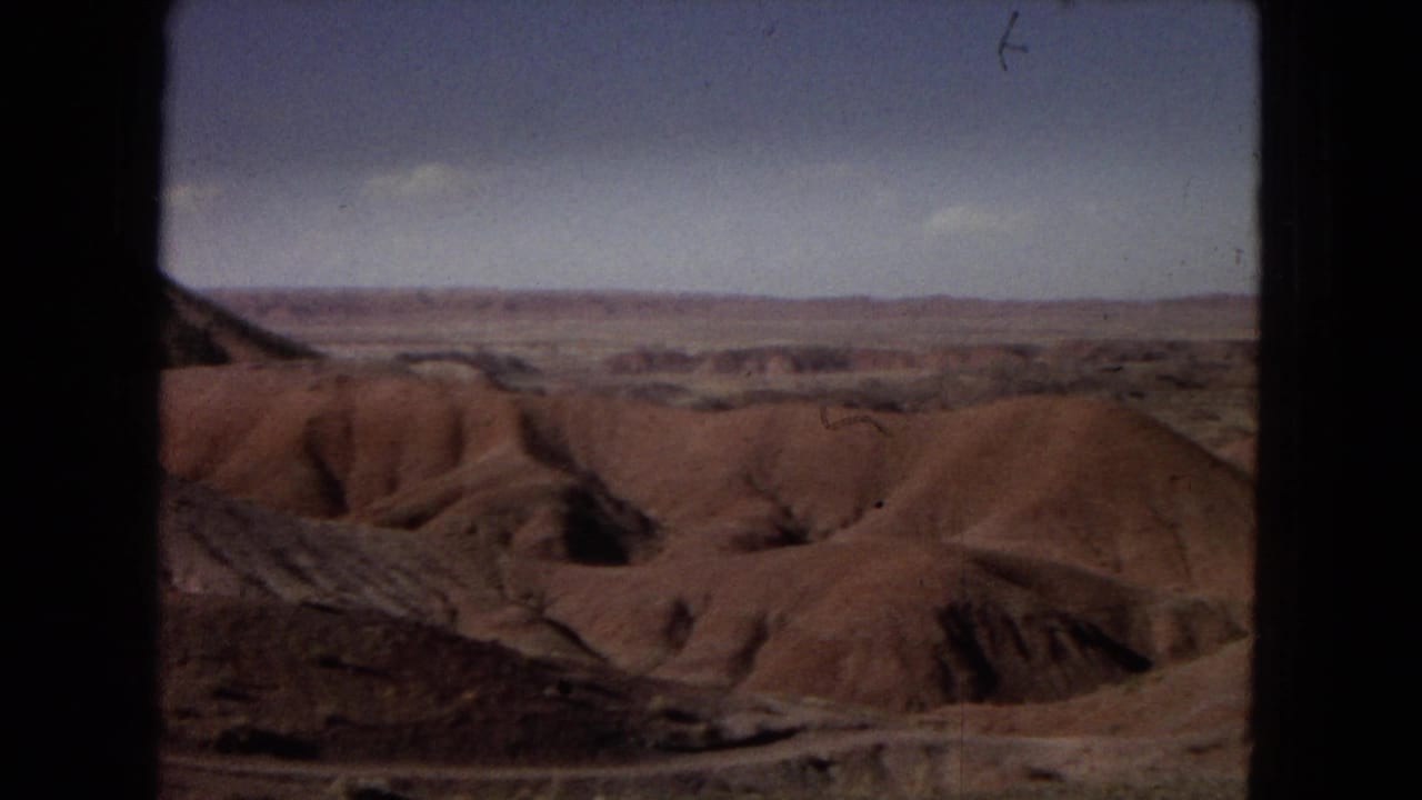 Arizona Painted Desert landscape with rounded badland mounds, shadowed gullies, and a broad horizon in a 1967 8mm home-movie frame.