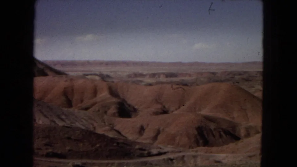 Arizona Painted Desert landscape with rounded badland mounds, shadowed gullies, and a broad horizon in a 1967 8mm home-movie frame.