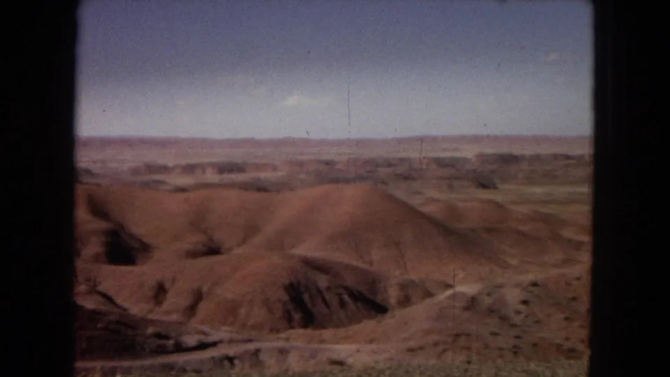 1967 Arizona desert panorama showing eroded badland forms, sparse scrub, and a flat distant horizon under daylight.