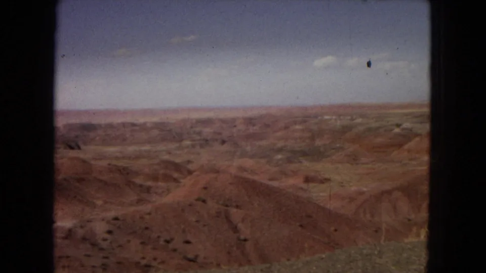 1967 Arizona 8mm view across red and brown desert formations with a low horizon, open sky, and dark film-frame borders visible at the edges.
