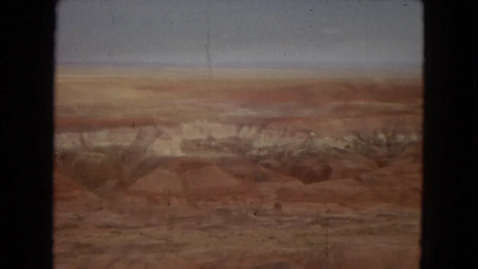 Final frame from the short pan showing a reddish desert basin, pale layered ridges, and open sky in vintage 8mm color.