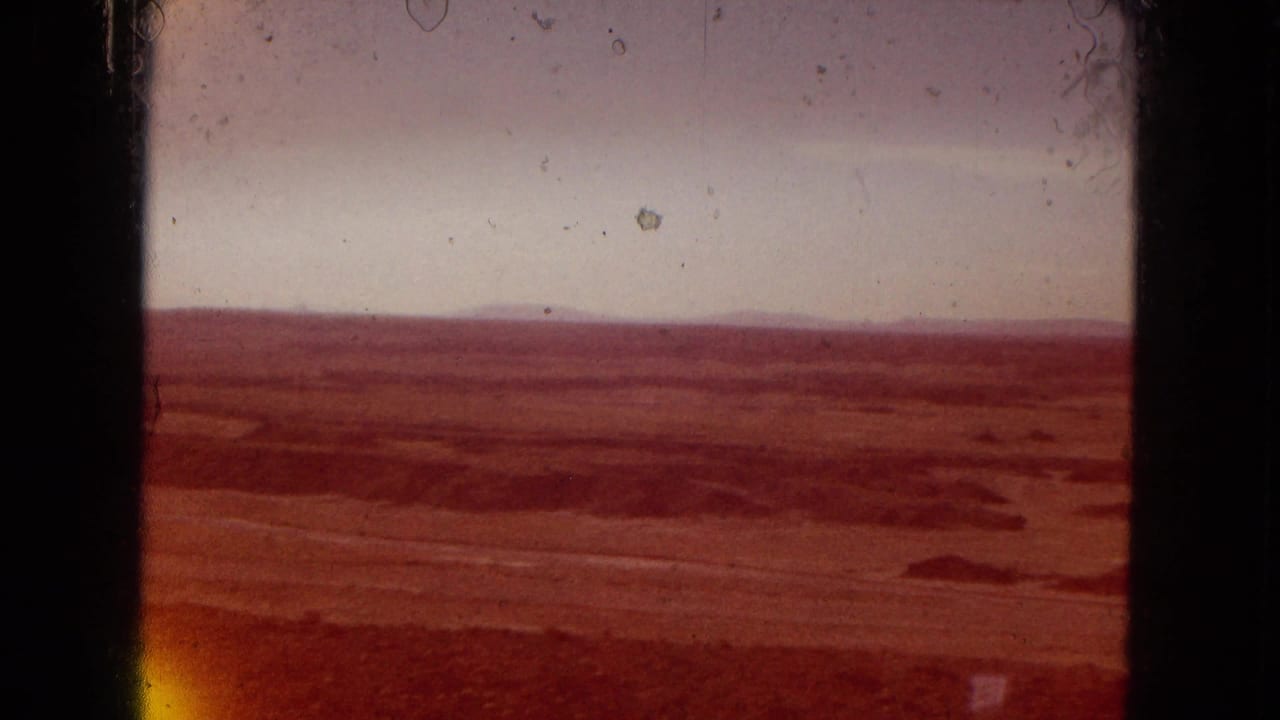 1967 Arizona home-movie frame showing a reddish cast over a broad arid valley, distant horizon, pale sky, and visible 8mm film artifacts.