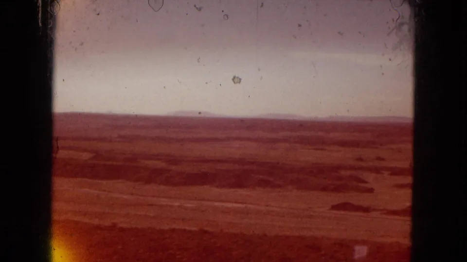1967 Arizona home-movie frame showing a reddish cast over a broad arid valley, distant horizon, pale sky, and visible 8mm film artifacts.
