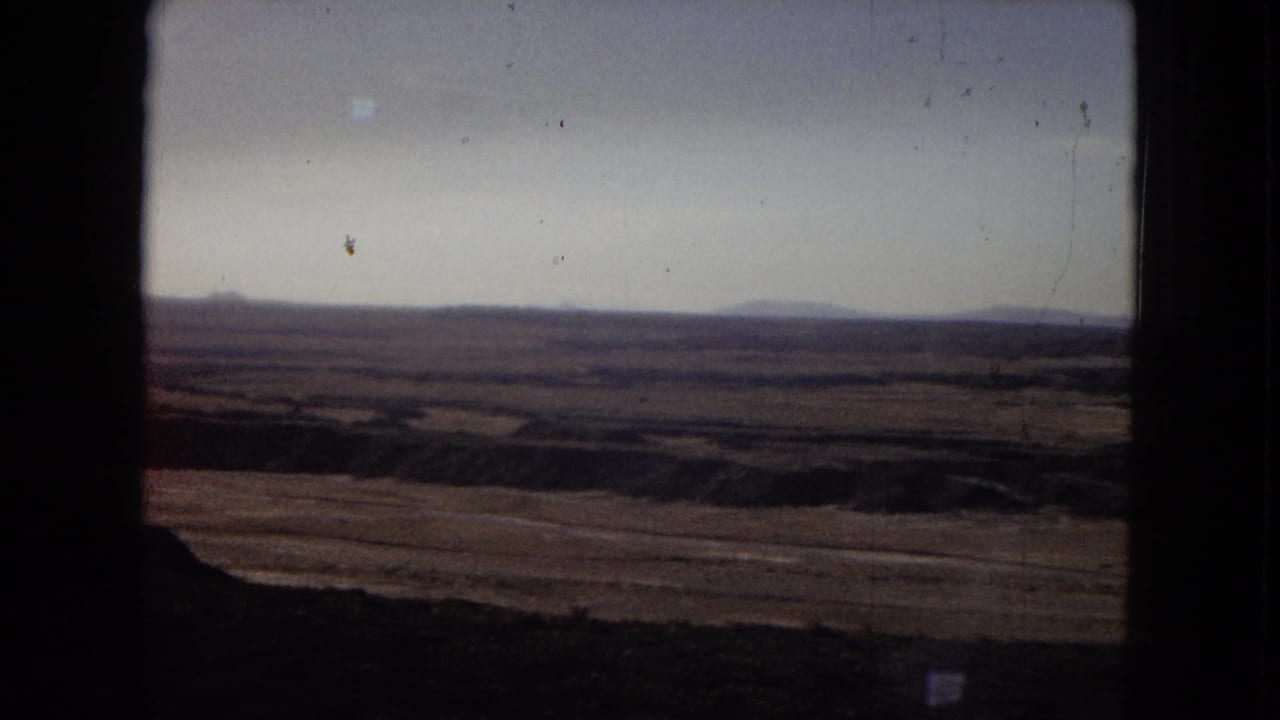 1967 Arizona travel-film view of a wide dry plain with distant low hills, muted color, and heavy vertical film-frame obstruction at the left edge.