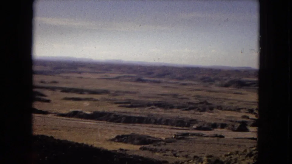 1967 Arizona 8mm view of an open arid valley with muted green-brown terrain, distant hills, pale sky, and heavy dark framing from the film or window edge.