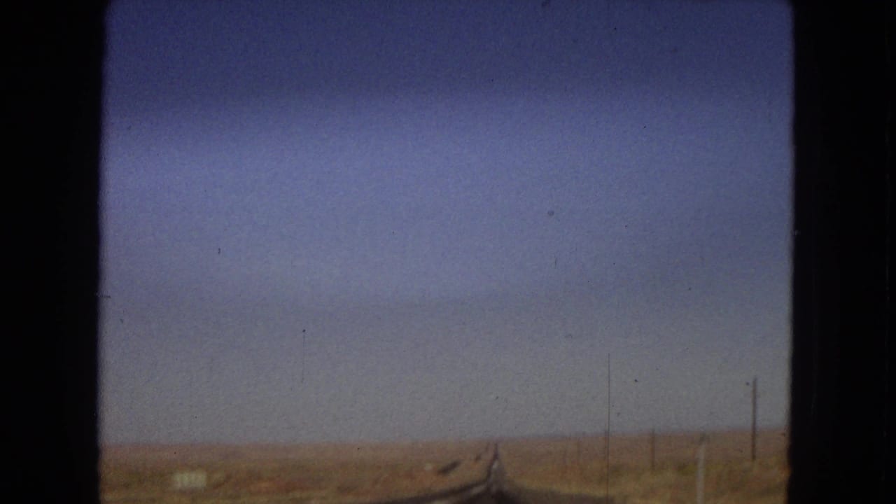1967 Arizona 8mm frame of a long straight roadway crossing flat arid land, with utility poles along the roadside and no visible people or vehicles nearby.