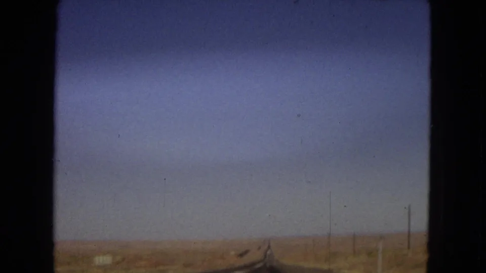 1967 Arizona 8mm frame of a long straight roadway crossing flat arid land, with utility poles along the roadside and no visible people or vehicles nearby.
