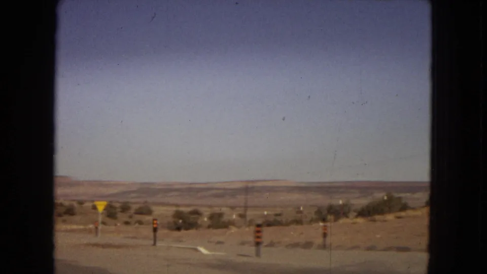 Arizona road-trip footage may show the highway shoulder and desert roadside, with yellow traffic signs, striped posts, low vegetation, and distant hills across the open landscape.
