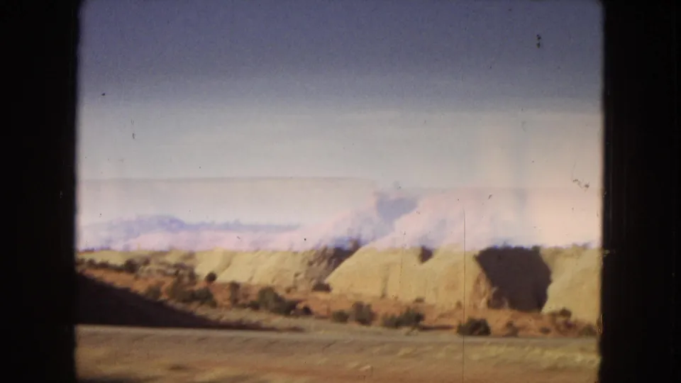 The final frame shows a desert roadway edge, eroded sandy hills, scrub vegetation, and distant bluish mountains in faded 8mm color from the 1967 Arizona travel clip.