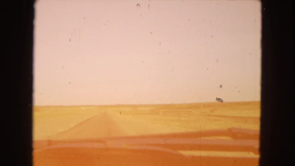 1967 Arizona home-movie view from inside a moving vehicle, looking through a dusty windshield toward a straight desert road and flat horizon.