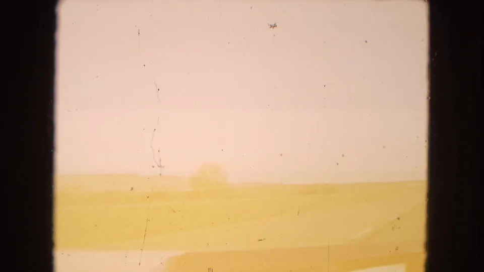 Faded 8mm frame of an Arizona desert drive, with a bright open horizon, faint road edge, windshield scratches, and distant indistinct trees or landforms.