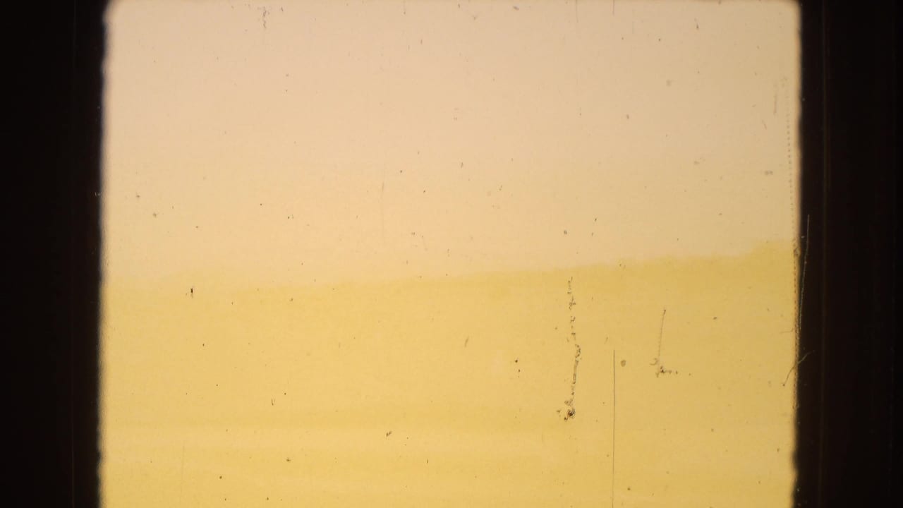 Warm, hazy 1967 Arizona desert horizon seen through a dark window-like frame, with pale sky, soft landforms, and visible 8mm dust and scratches.