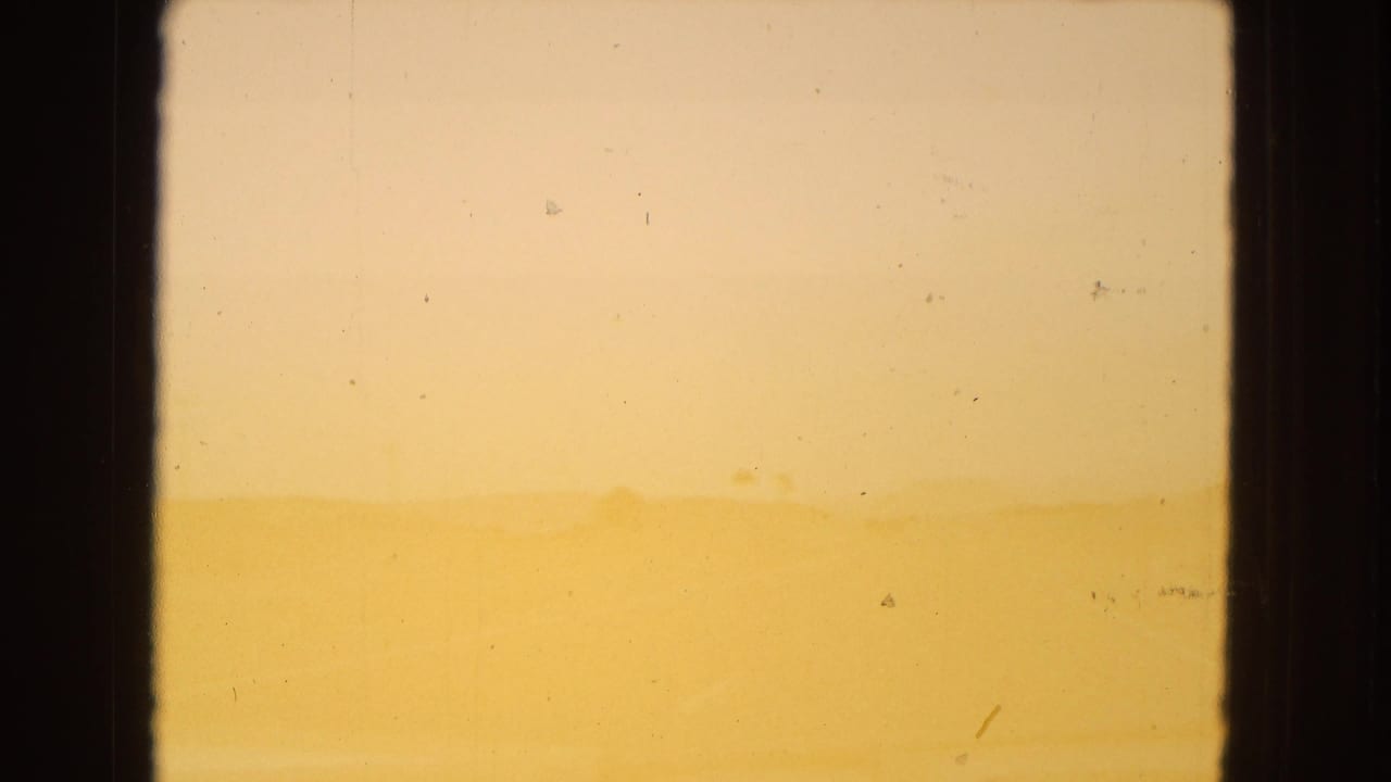 Faint Arizona desert ridge beneath a pale yellow sky, bordered by dark film or window edges and marked by light 8mm surface wear.
