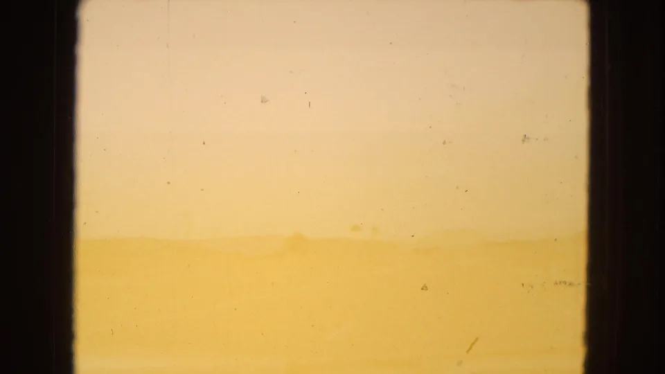 Faint Arizona desert ridge beneath a pale yellow sky, bordered by dark film or window edges and marked by light 8mm surface wear.