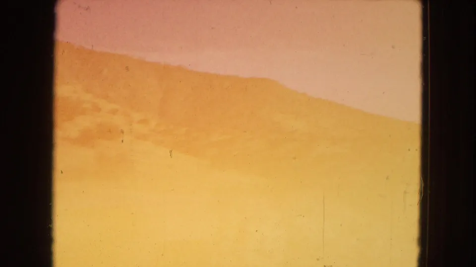 1967 8mm home-movie frame from Arizona showing a bright, overexposed roadside hillside seen through the dark edge of a moving car window.