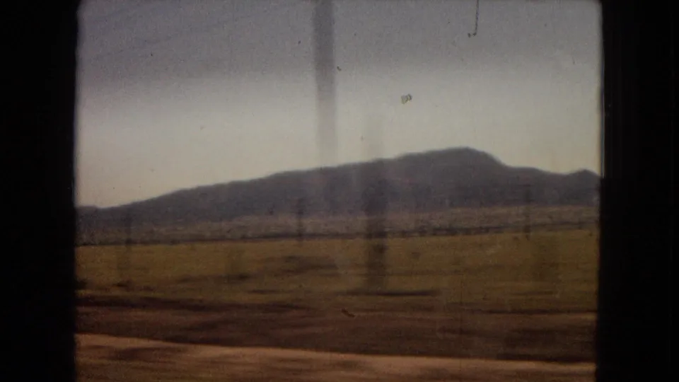 1967 home-movie frame looking across flat open land toward distant low mountains, with visible 8mm softness and color fading.