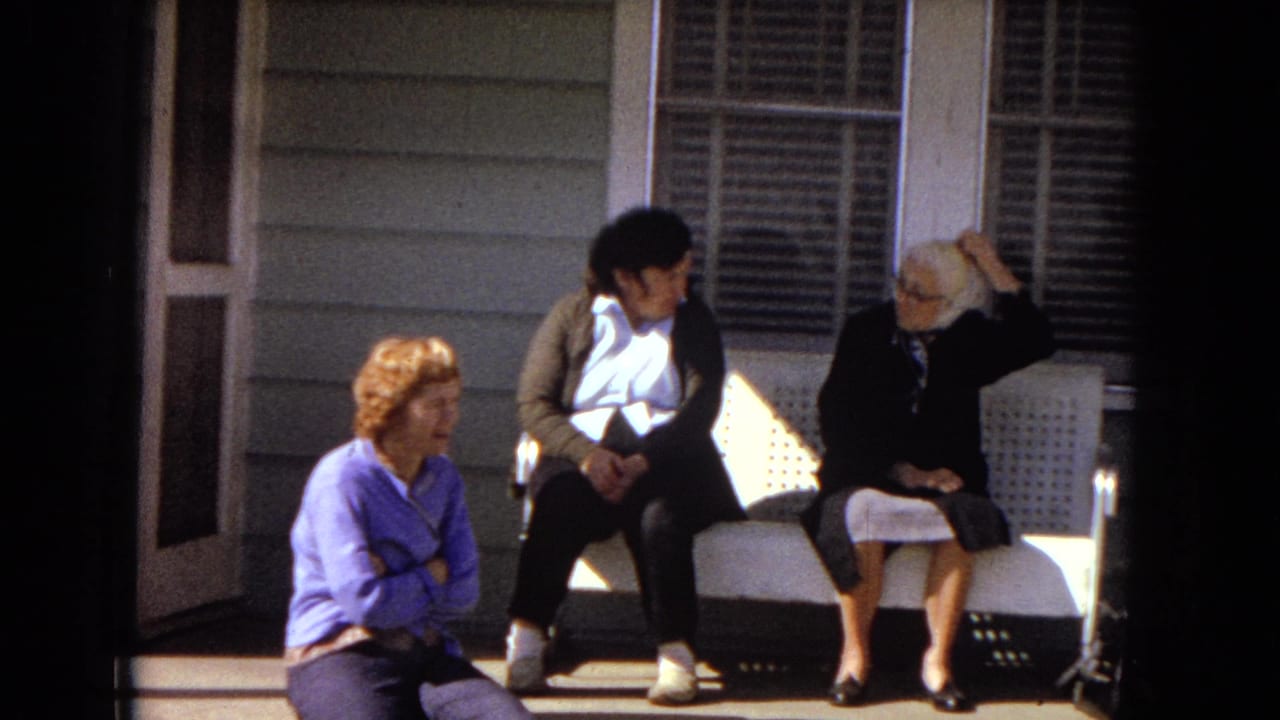 In 1967 Arizona home-movie footage, three women from different generations sit on a front porch, with one on the steps and two on a white bench beside shuttered windows.
